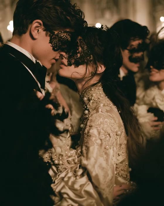 A masked couple in an embrace, she in gold embroidered tulle, he in a black tuxedo